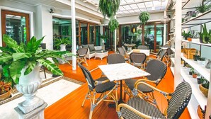 An indoor patio area with wicker furniture, potted plants, and a glass ceiling.