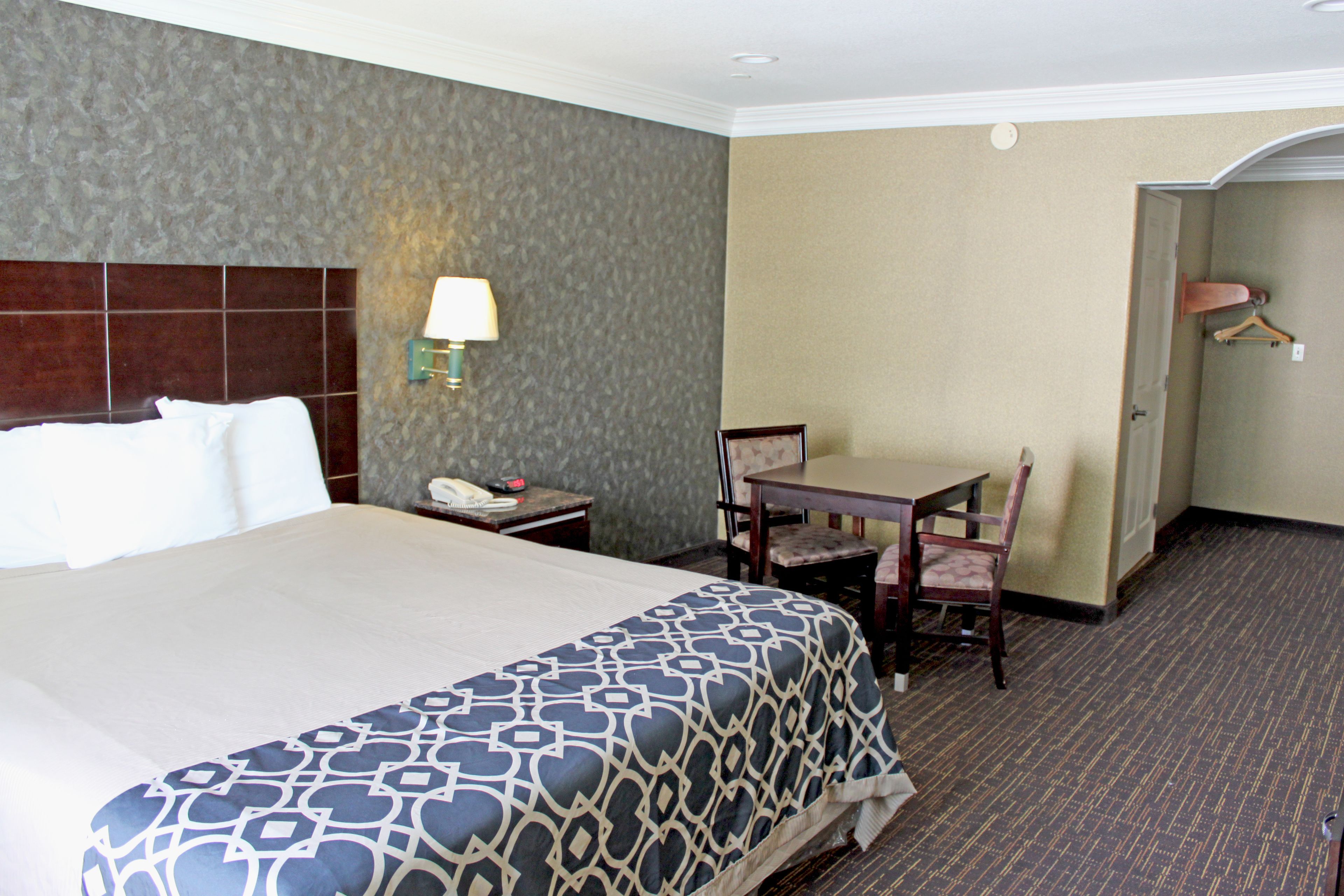 A hotel room with a large bed, a desk, a chair, a lamp, and a coat rack.