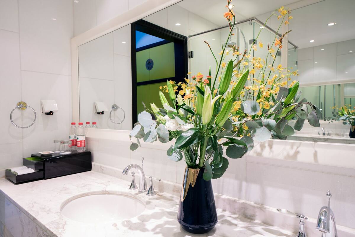 A bathroom with a marble sink, a large mirror, and a vase of flowers.