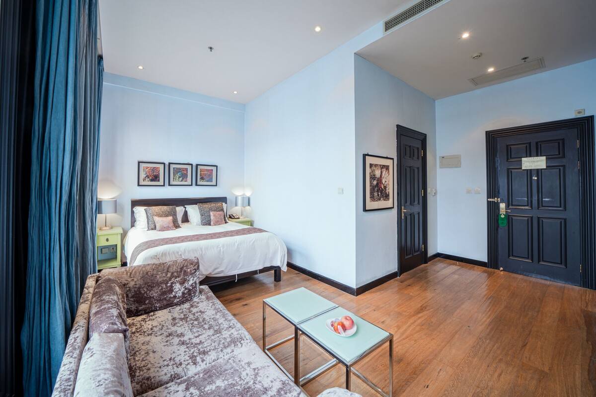 A hotel room with a bed, a sofa, a small table, and artwork on the walls.