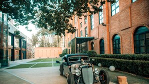 Un coche antiguo estacionado en un patio con edificios de ladrillo y un césped verde.