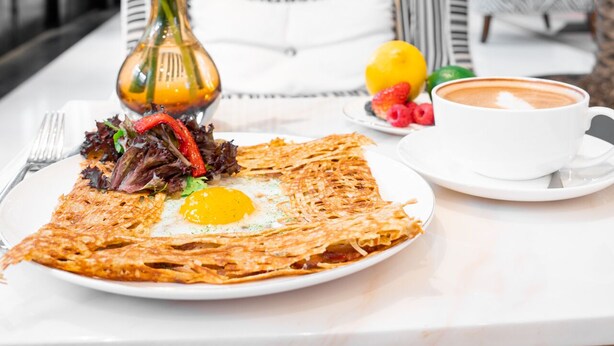 Un desayuno con un plato de comida, una taza de café y un florero con plantas verdes.
