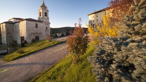 A historic building with a bell tower, a paved road, and a coniferous tree. - Hotel San Antón Abad (Villafranca Montes de Oca)