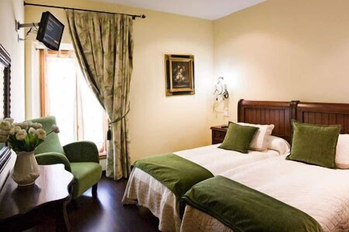 Une chambre à coucher avec un lit double, deux tables de chevet, une chaise, un bureau, une télévision et un tableau au mur.