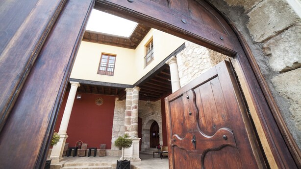 A courtyard with a wooden door, stone columns, and a red door. - Hotel San Antón Abad (Villafranca Montes de Oca)