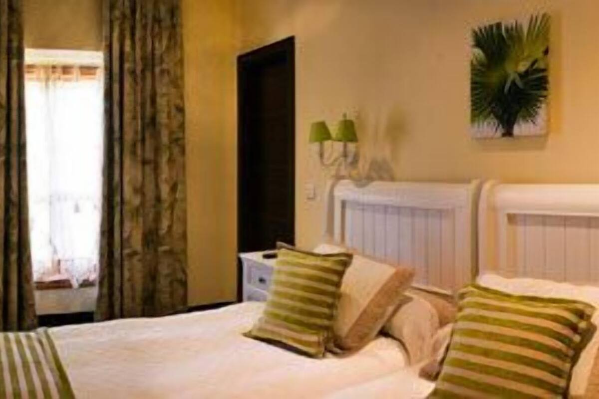 Une chambre d’hôtel avec un lit, des tables de chevet, un miroir, un radiateur et une fenêtre avec des rideaux.