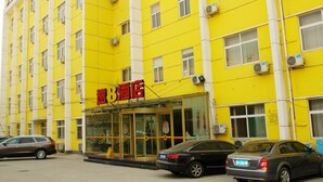 A yellow building with multiple windows and air conditioning units. There is a sign with red characters and a glass door entrance. Two cars are parked in front. - Super 8 Hotel- Jinan Coach Station Branch (Jinan)