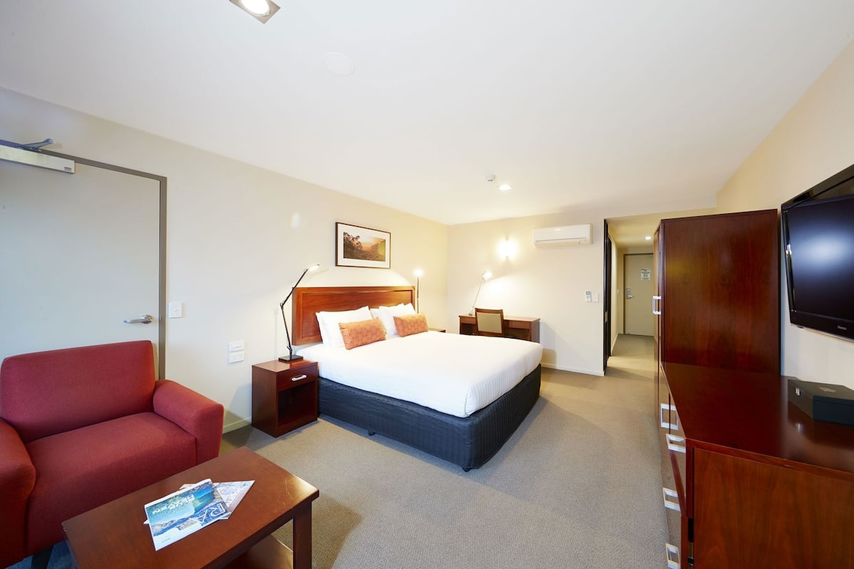 A hotel room with a bed, a desk, a chair, a TV, and a door.