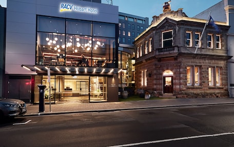 A RACV Hotel with a modern glass facade and a traditional stone building adjacent to it.