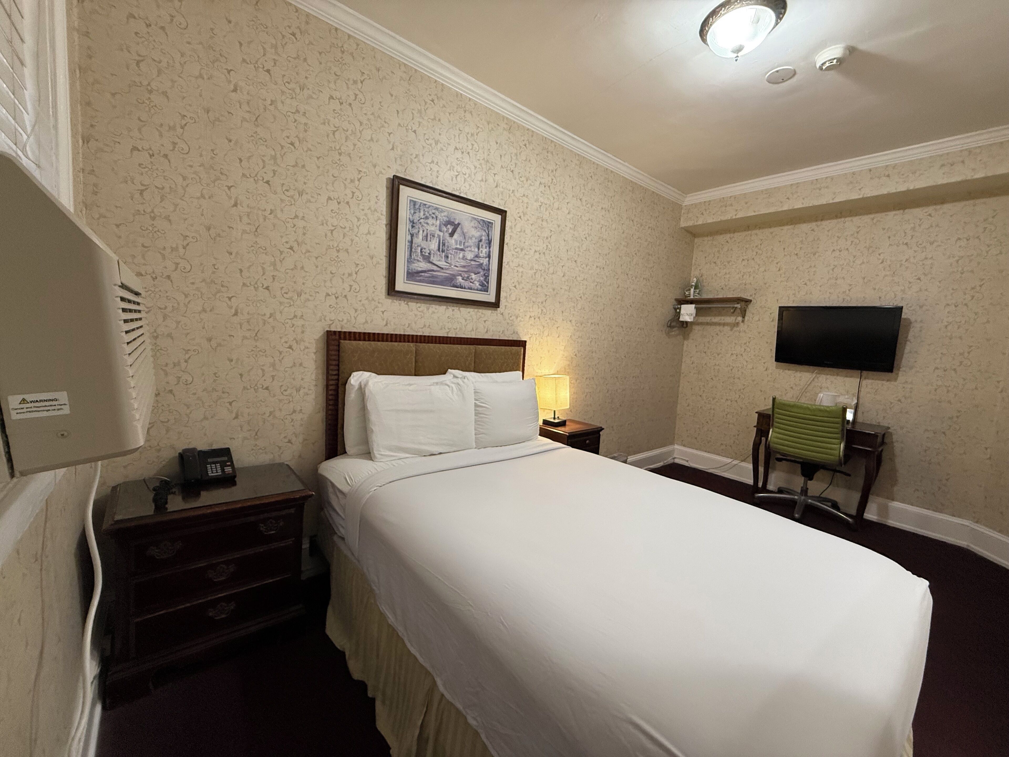 Une chambre d’hôtel comprenant un lit, une table de chevet, une lampe, un téléviseur et une chaise.
