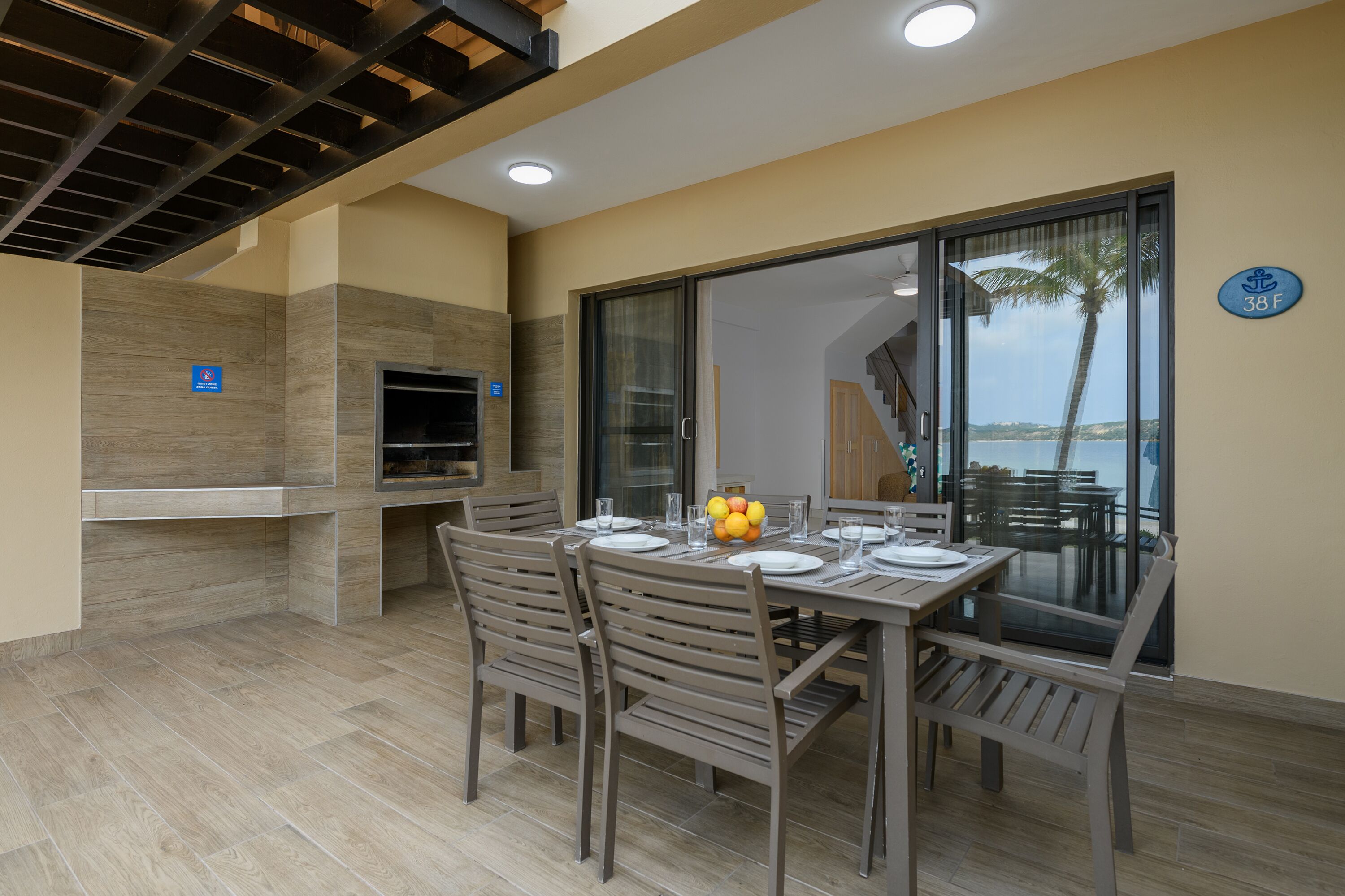 A dining area with a table set for four, a grill, and a view of the sea.