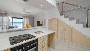 A modern kitchen with a large island, a built-in oven, and a view of the sea through large windows.