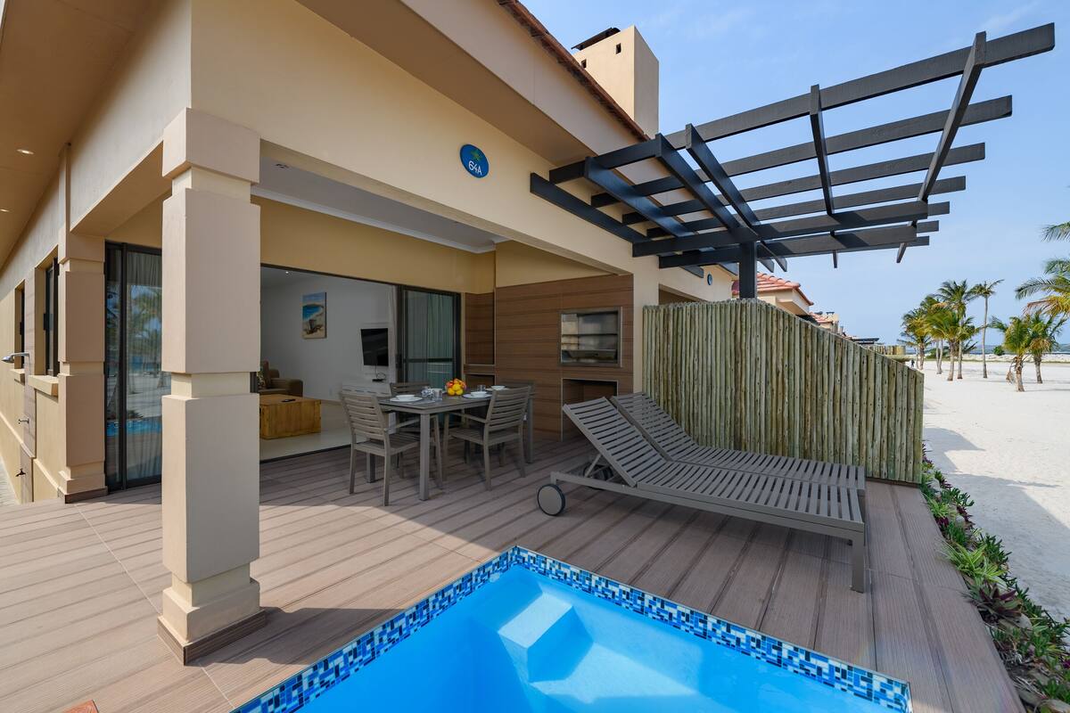 Un espace piscine extérieur moderne, doté d’une terrasse en bois, d’une chaise longue et d’une table à manger avec des chaises.