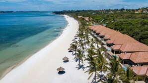 A beach resort with a long row of rooms along the shoreline, clear blue water, and palm trees.