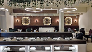 Un espace d’accueil moderne avec un mur en briques, des panneaux décoratifs à motifs floraux et un comptoir de buffet proposant divers plats et boissons.