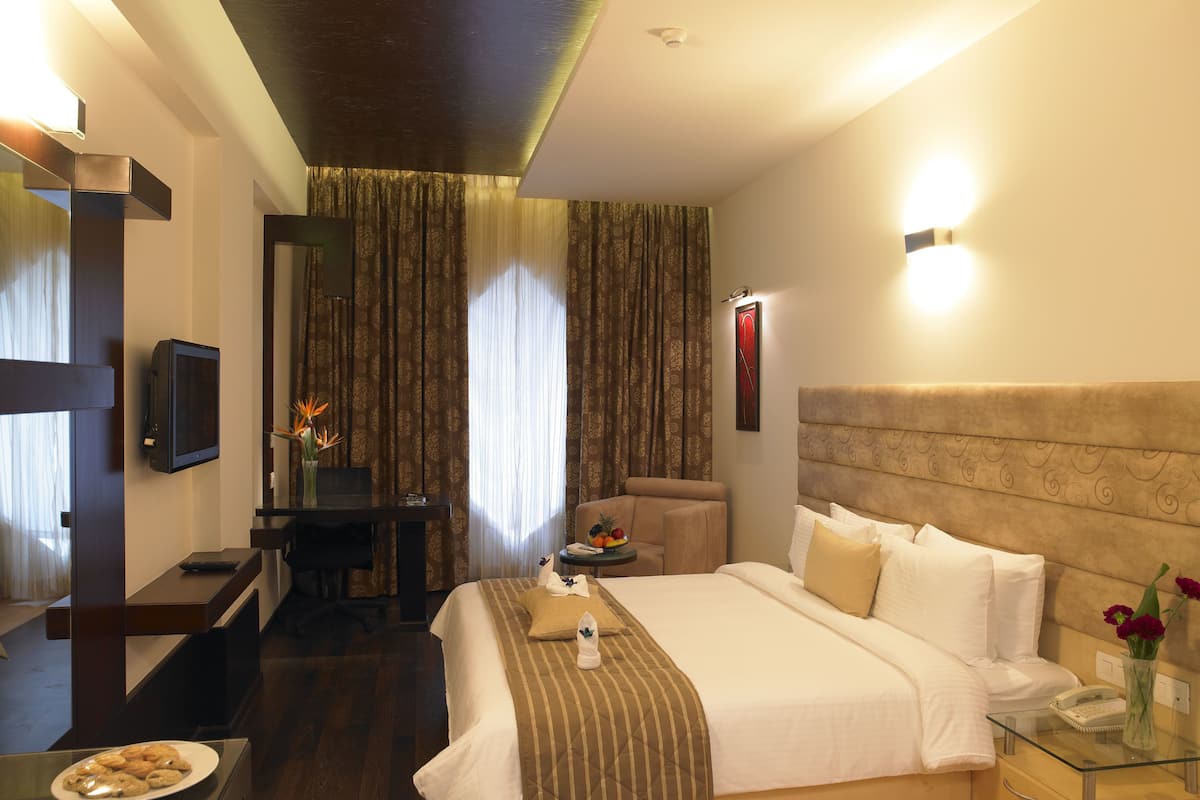 A hotel room with a bed, bedside table, desk, chair, and a television.