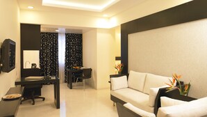 Une chambre d’hôtel moderne équipée d’un canapé, d’un bureau avec un ordinateur, d’une chaise et d’un coin repas comprenant une table et des chaises.