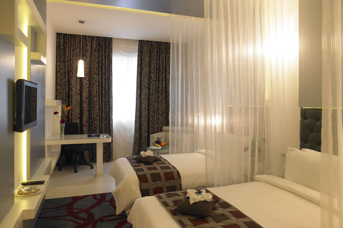 A hotel room with a bed, a desk, a chair, a TV, and a window with curtains.