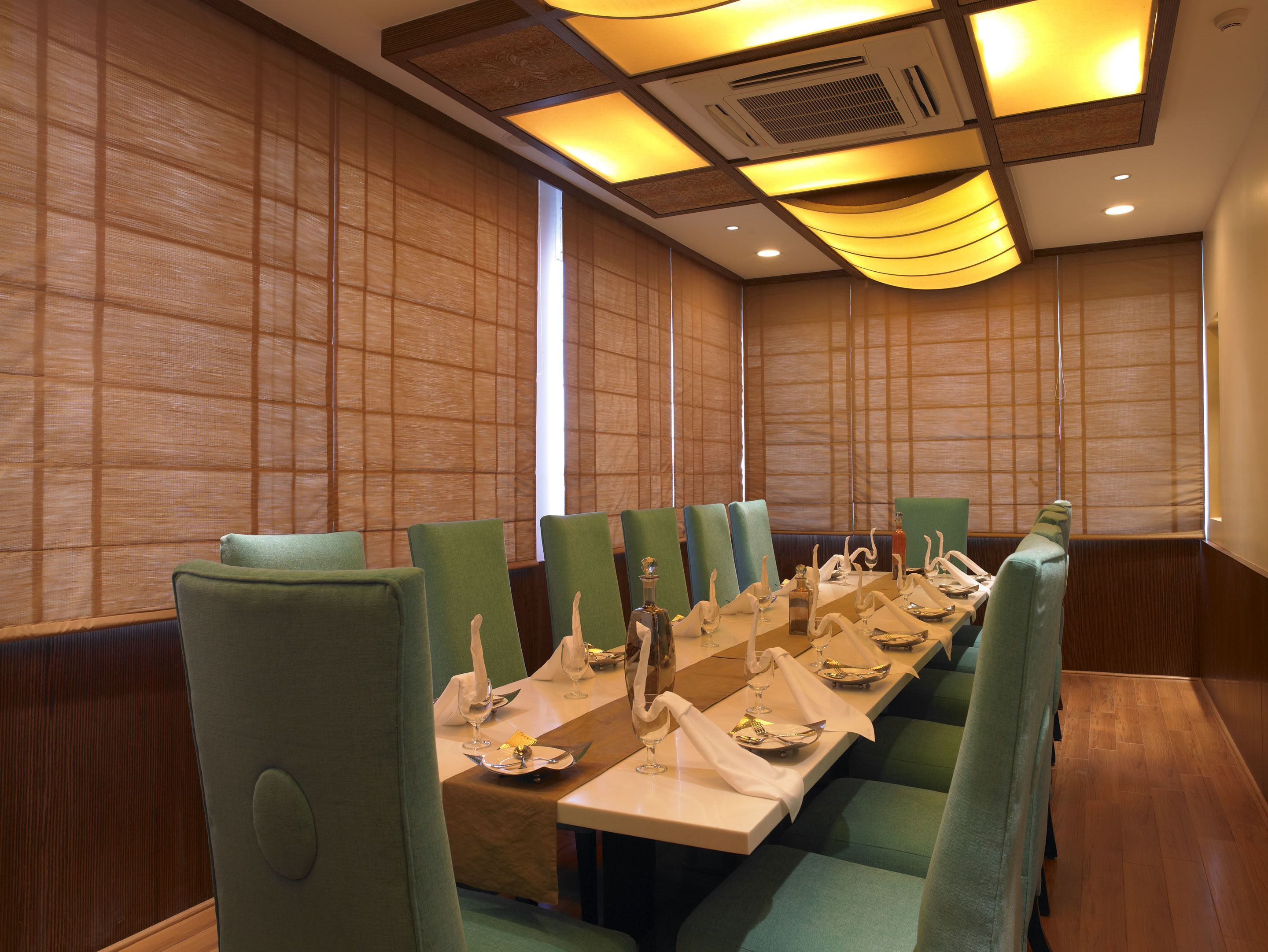 A conference room with a long table set for a meeting, surrounded by green upholstered chairs.
