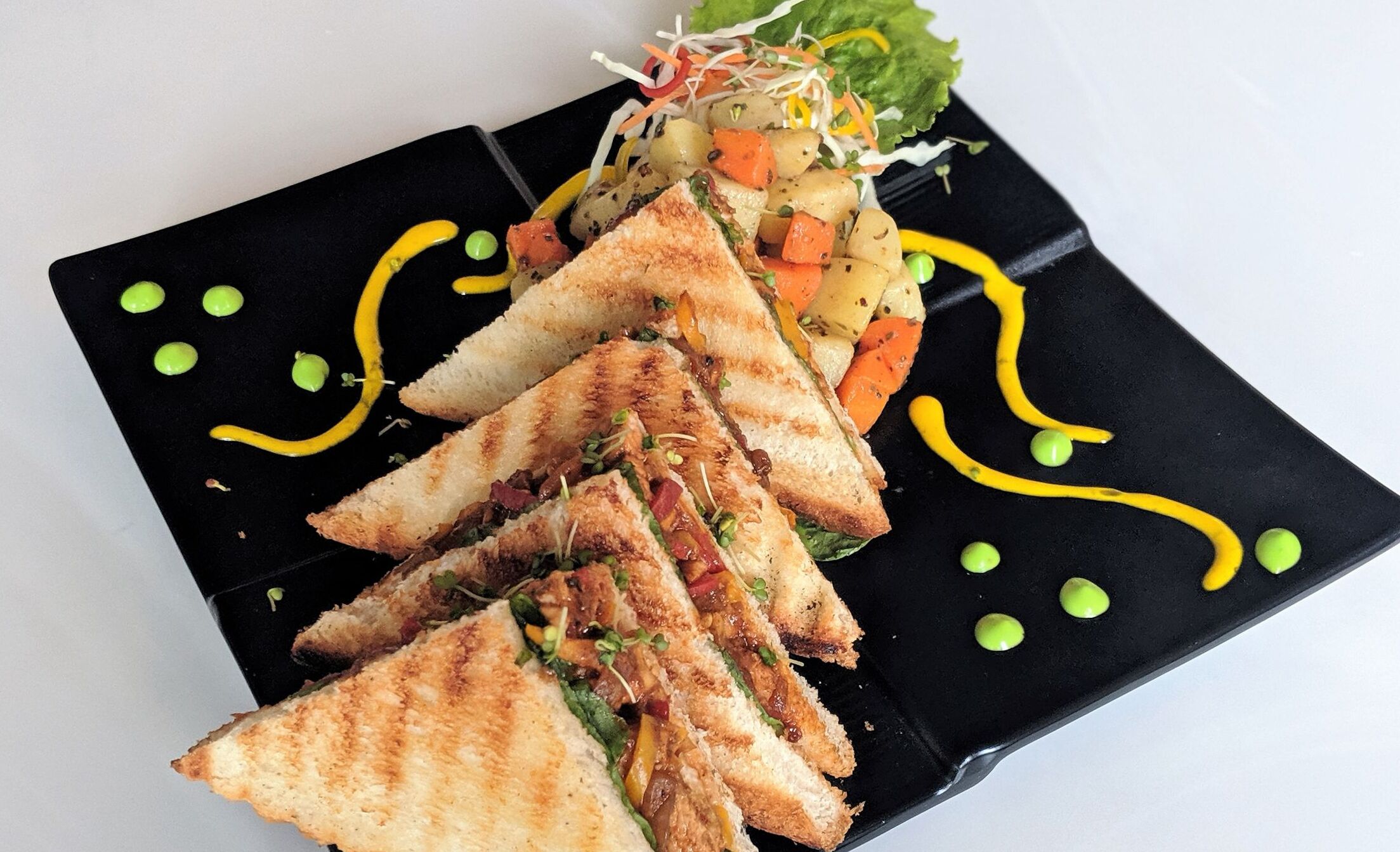 A black plate with grilled sandwiches, a side salad, and decorative yellow and green dots.