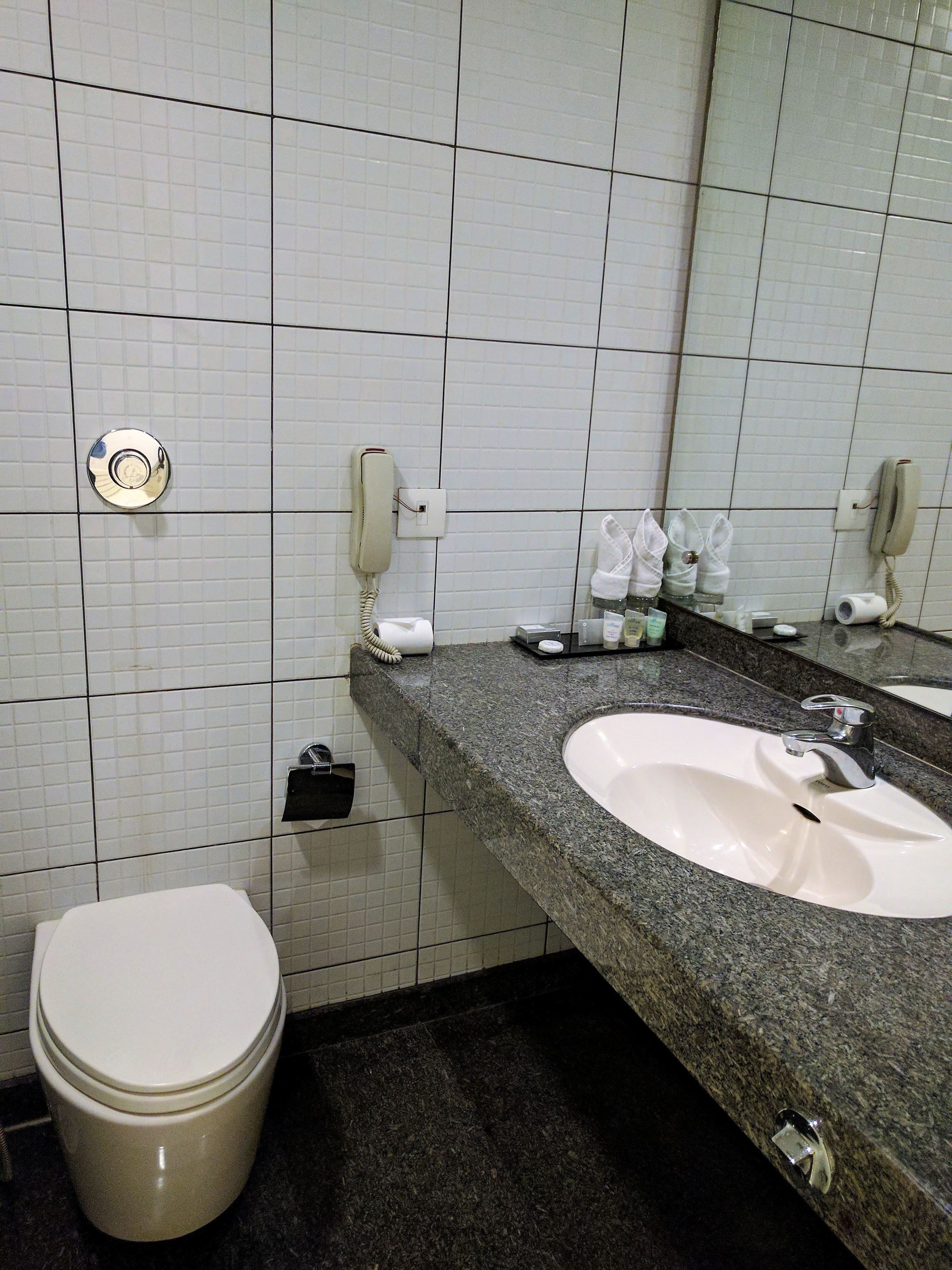 A bathroom with a white toilet, a sink with a mirror, and two phones mounted on the wall.