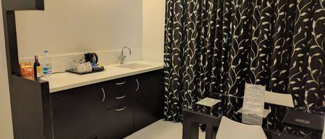 Un bagno moderno con una tenda da doccia a motivi foglia bianchi e neri, un lavandino bianco e un piccolo tavolino con una sedia.
