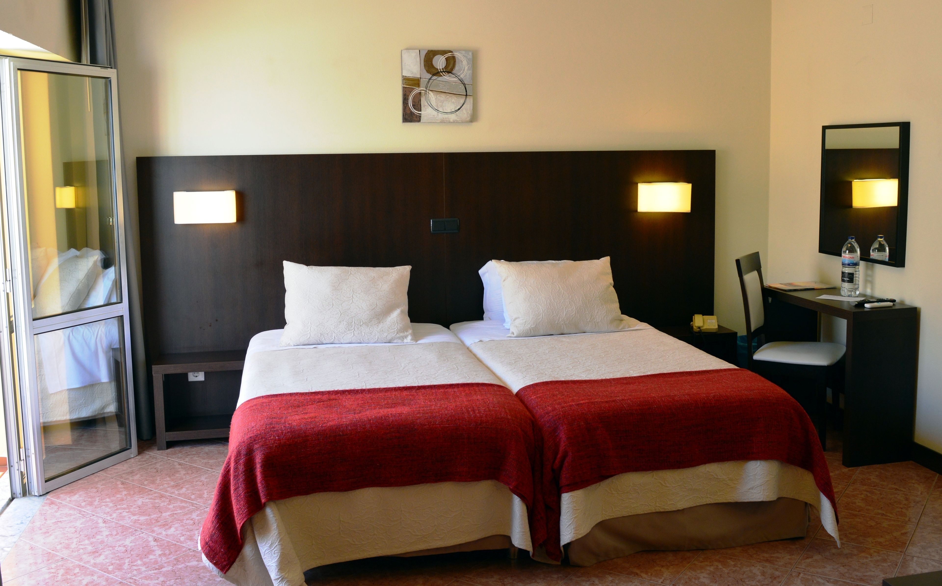 Hotellihuone, jossa on kaksi sänkyä, työpöytä, tuoli, peili ja seinälle kiinnitetty taideteos.