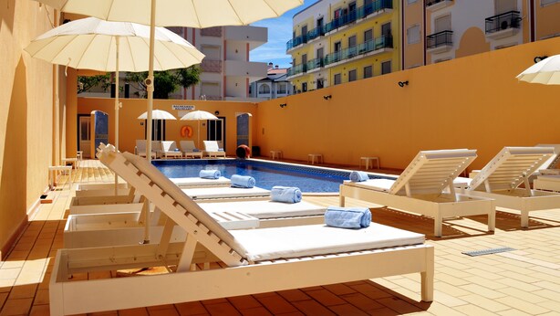 A poolside area with sun loungers, umbrellas, and a pool. - Hotel Apolo (Vila Real Santo Antonio)