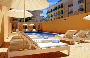 Zona junto a la piscina con tumbonas, sombrillas y una piscina.