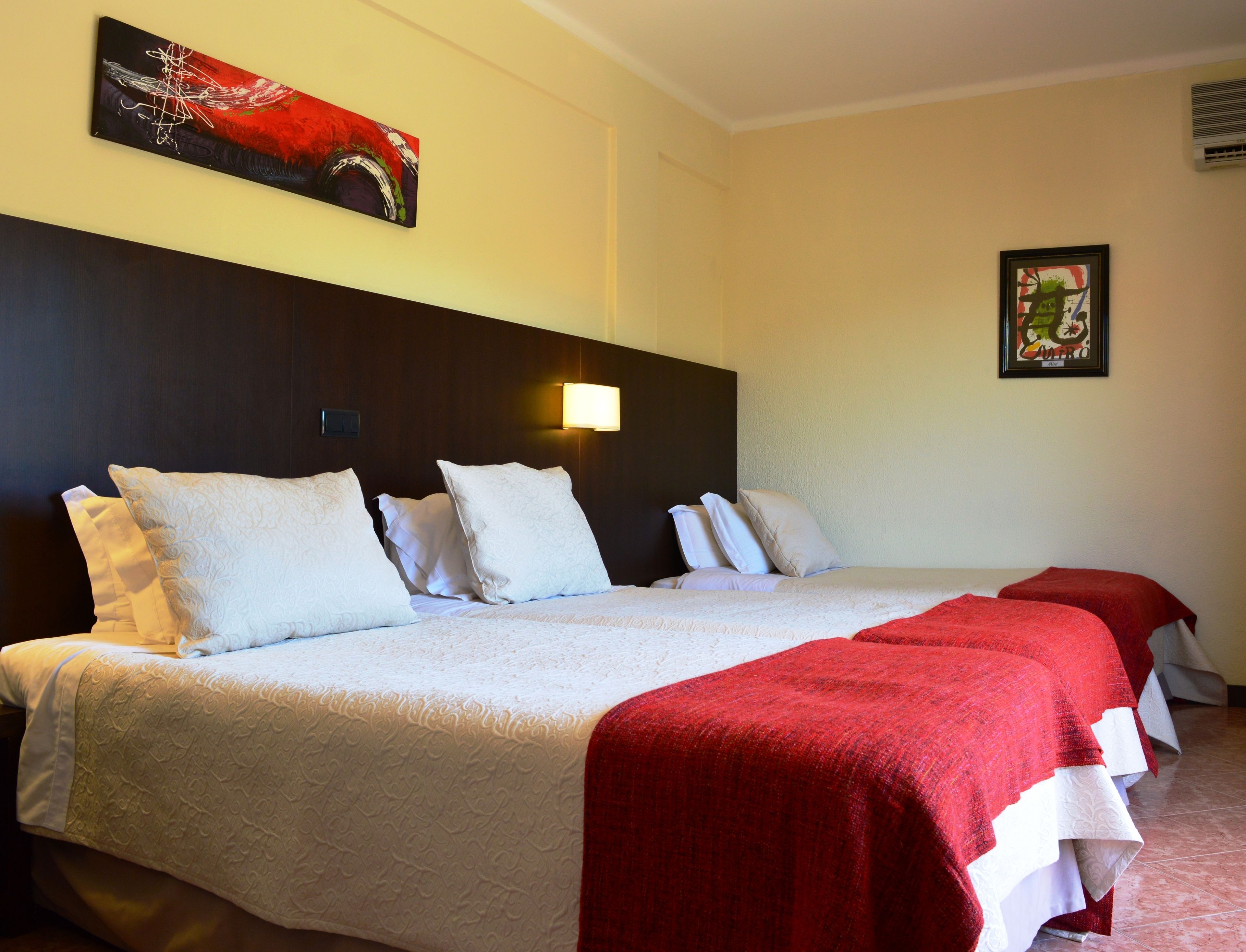 Une chambre d’hôtel avec un grand lit, plusieurs oreillers, une couverture rouge et deux appliques murales.