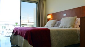 A hotel room with a large bed, a wooden headboard, and a view of the city through a sliding glass door. - Hotel Apolo (Vila Real Santo Antonio)