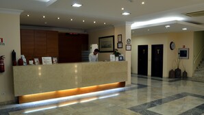A hotel reception area with a marble floor, a reception desk, framed artwork, and a staircase. - Hotel Apolo (Vila Real Santo Antonio)