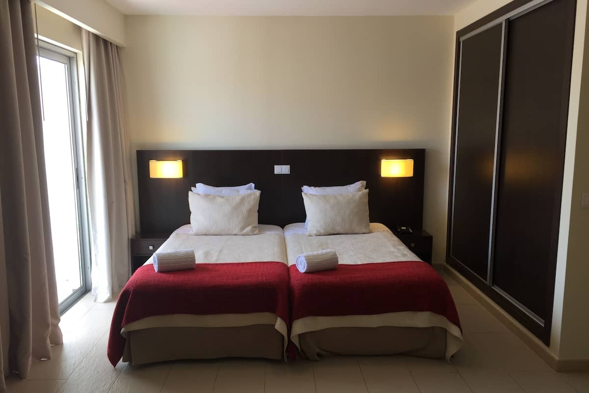 A hotel room with two beds, each with a red bedspread and white pillows, a dark headboard, and two bedside lamps.