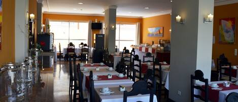 A restaurant with multiple tables and chairs, a buffet area, and a television mounted on the wall.