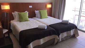 A hotel room with two beds, each with a white and green pillow, a wooden headboard, and a nightstand with a lamp.