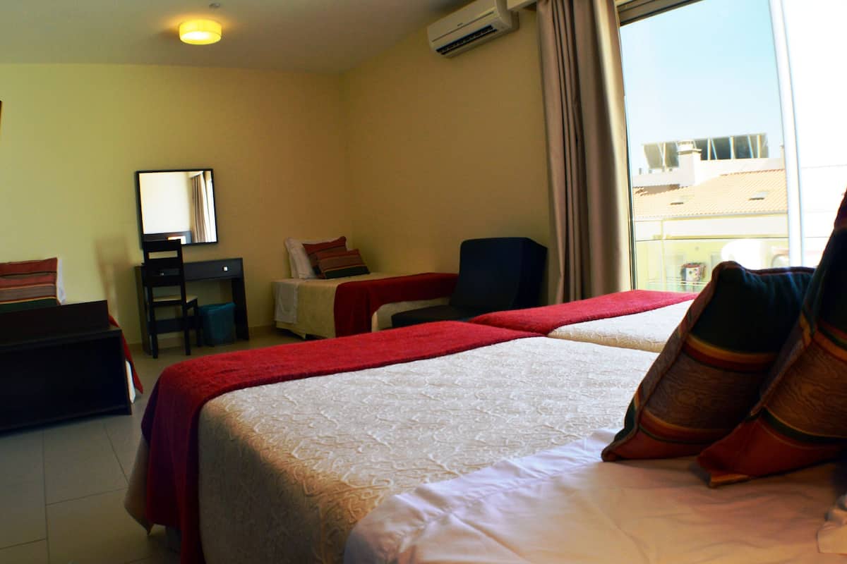A hotel room with two beds, a desk, a chair, a TV, and a window with a view of buildings.