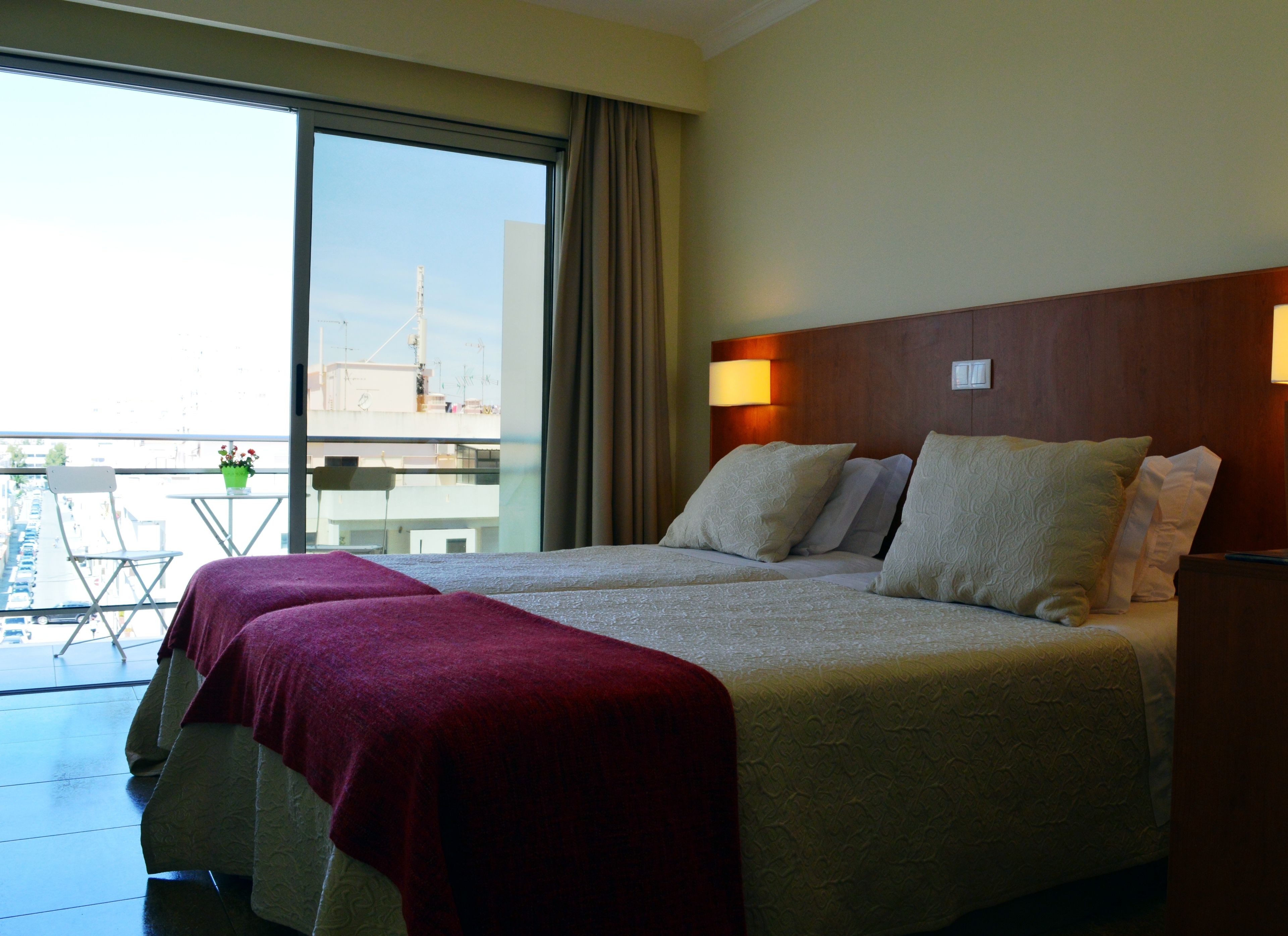 Habitación de hotel con una cama grande, un balcón con vistas a la ciudad y una mesita con una planta.