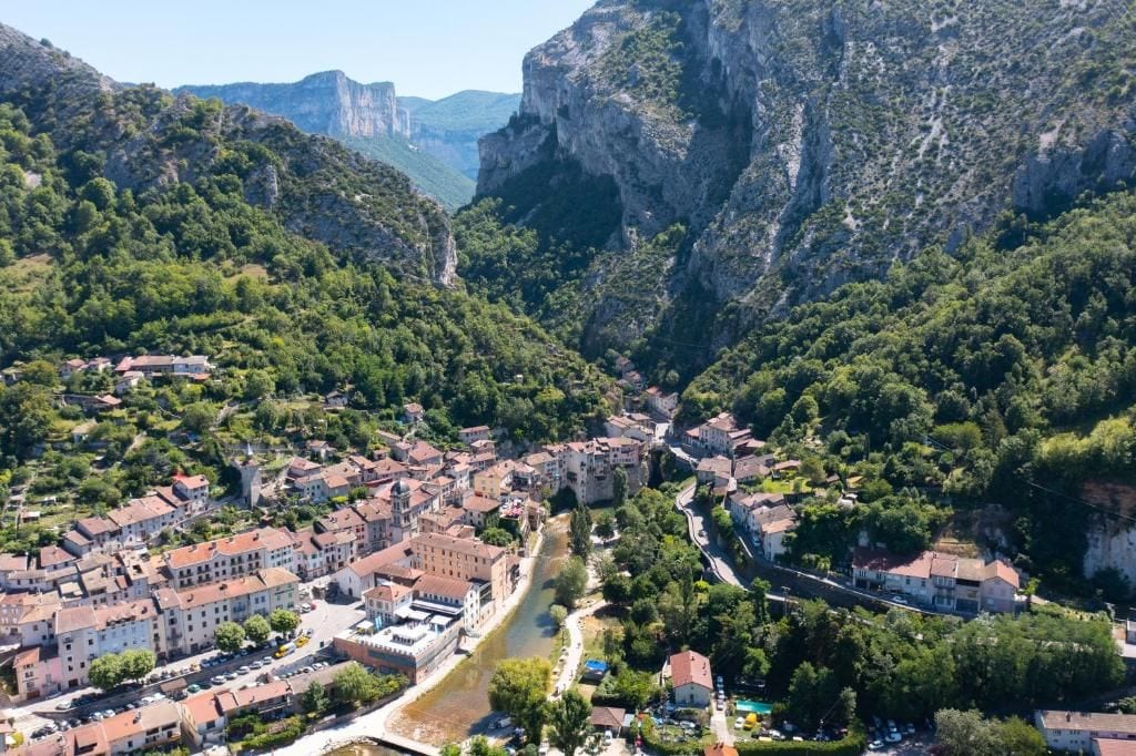 Uma cidade aninhada num vale, com um rio serpenteando por ela, rodeada por penhascos íngremes.