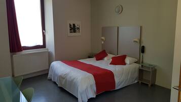 Une chambre d’hôtel bien aménagée, avec un grand lit, une table de chevet avec une lampe, un téléphone et une petite table avec une chaise.