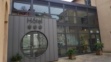 L’entrée d’un hôtel, avec une façade moderne, de grandes fenêtres et une porte circulaire en verre.