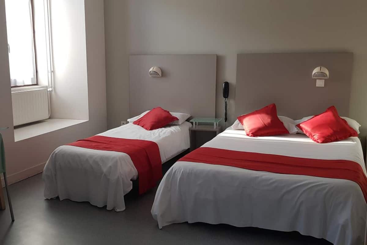 Habitación de hotel con dos camas, cada una con ropa de cama roja y blanca, un escritorio con silla, un televisor montado en la pared y una ventana que proporciona luz natural.