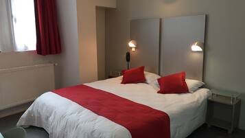 Ett hotellrum med en stor säng, röda kuddar, ett sängbord med en lampa och en telefon som är monterad på väggen.