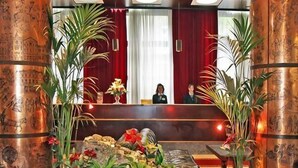 En lobby med en receptionsdisk, to store bronzekolonner, et siddeområde med læderstole og en dekorativ plantearrangement.