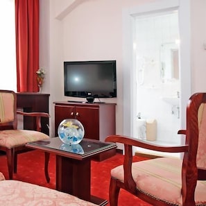 Habitación de hotel con una televisión sobre un soporte de madera, un pecera de vidrio sobre una mesita y dos sillones tapizados.