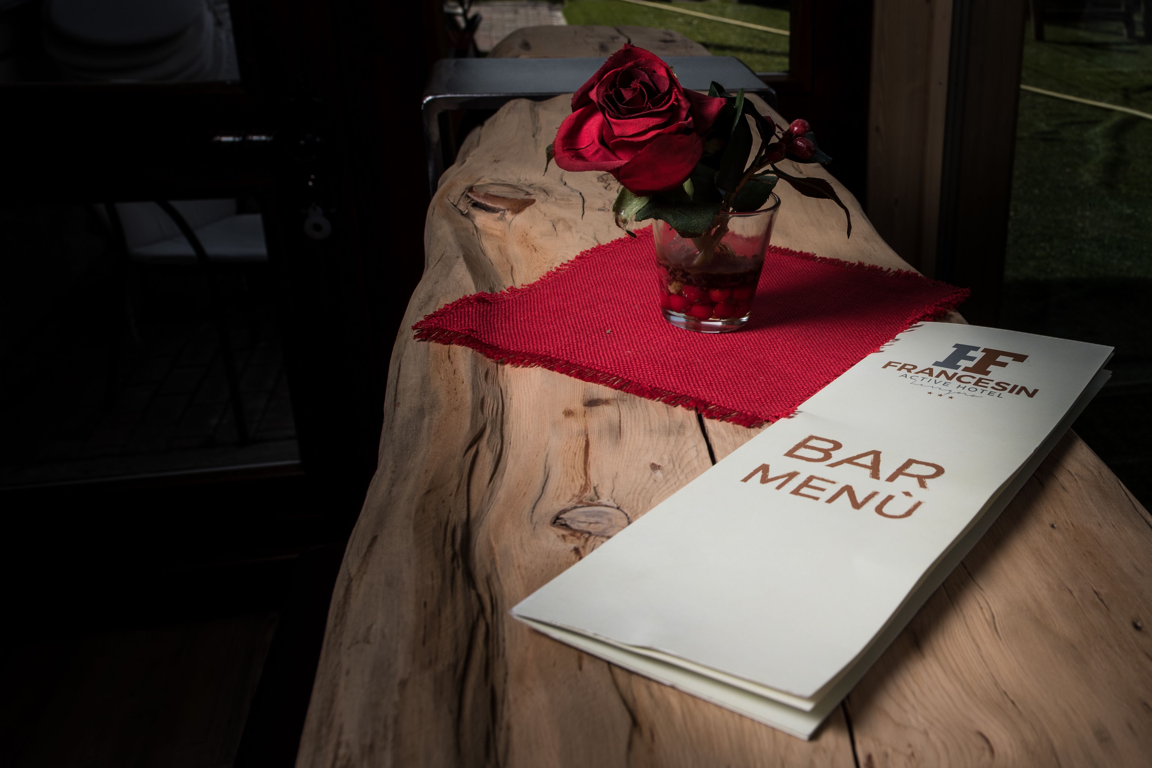 A wooden table with a red placemat, a glass of water, a red rose, and a menu titled "BAR MENU" from the "FRANCE HOTEL".