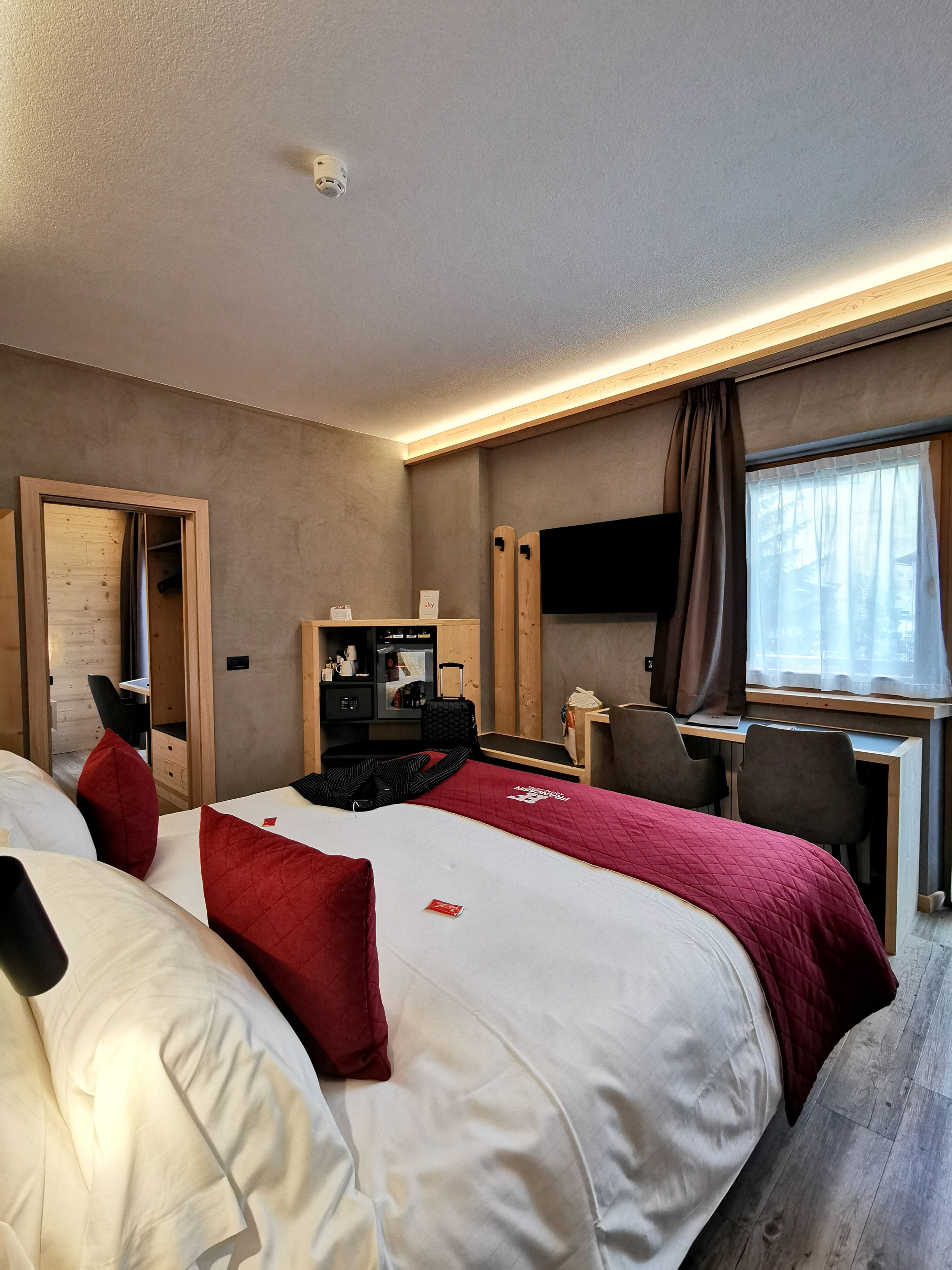 A hotel room with a bed, a desk, a chair, a television, and a window with curtains.