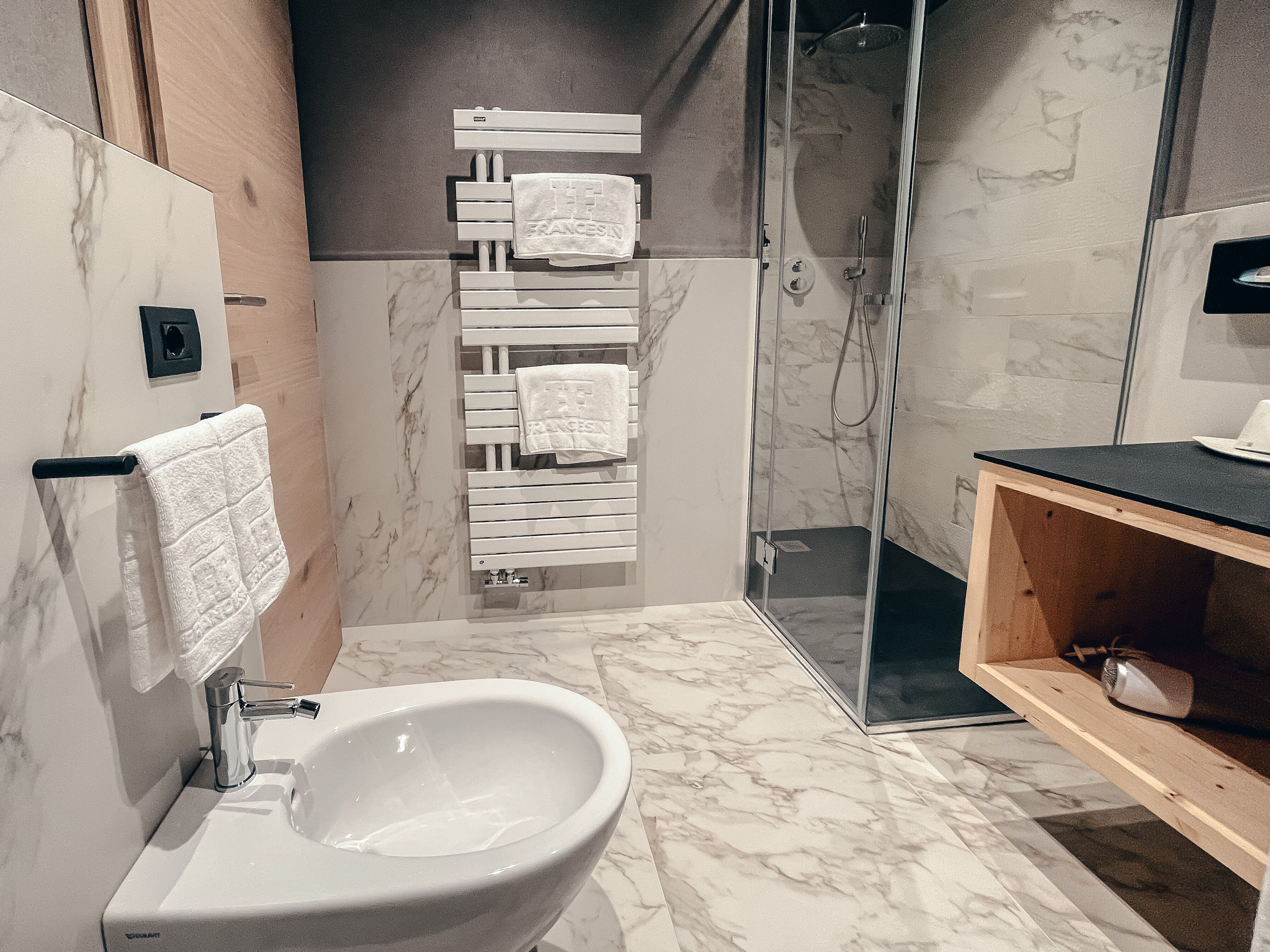 Un baño moderno con lavamanos de mármol, cabina de ducha de vidrio y tocador de madera.