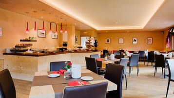 Una spaziosa sala da ristorante con diversi tavoli e sedie, un bancone con prodotti alimentari e lampade a sospensione.