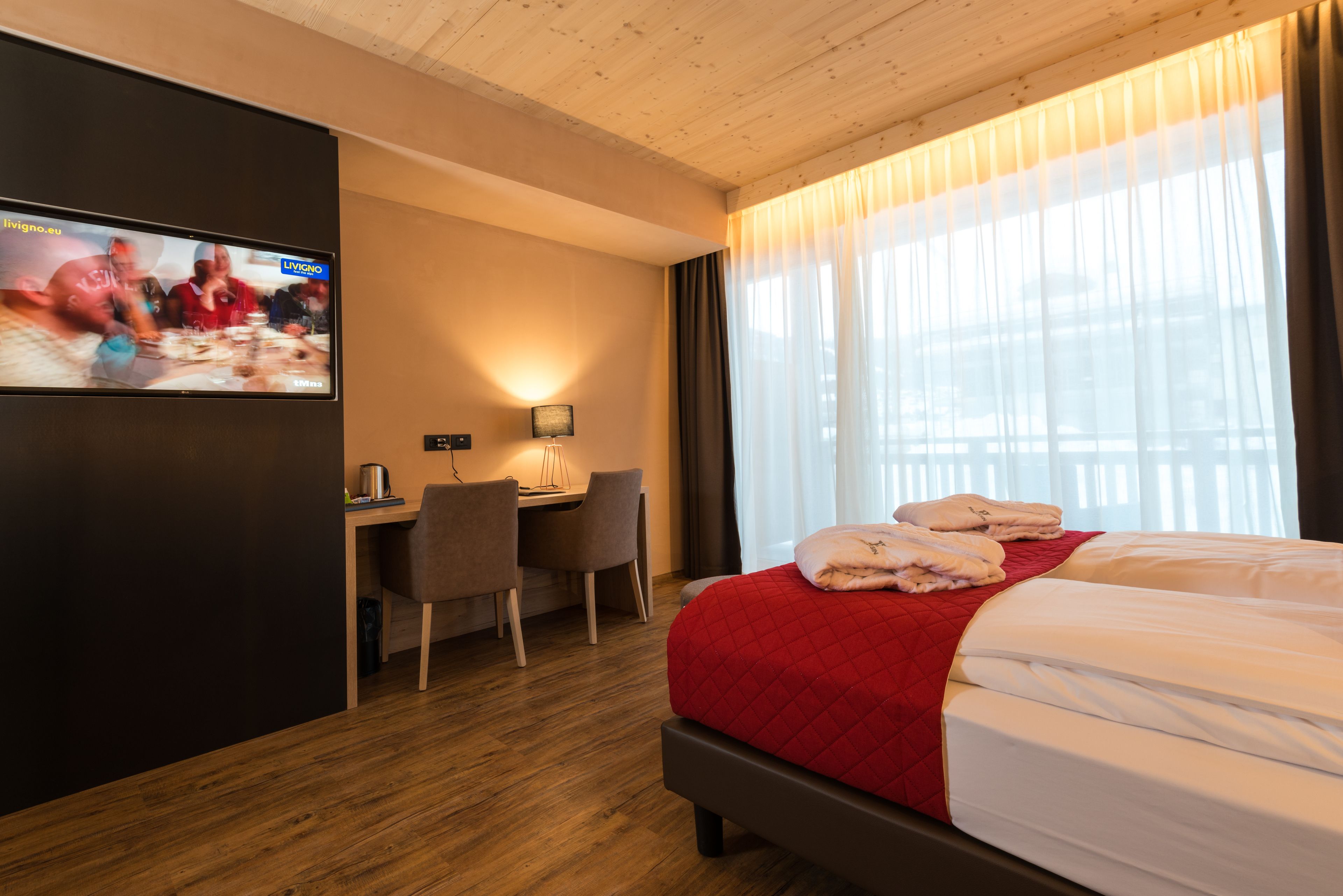 A hotel room with a bed, a desk, a chair, a TV, and a window with curtains.