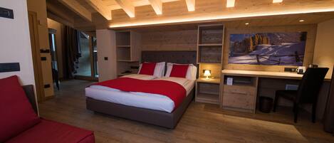 A modern bedroom with a large bed, a desk, and a chair. There is a painting on the wall and a wooden ceiling.